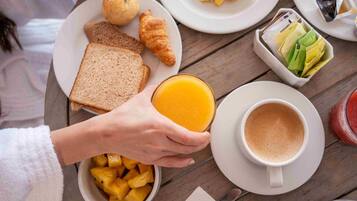 Mesa de madeira com pão tostado, croissants, frutas e uma xícara de café.
