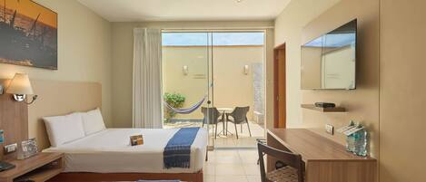 Habitación de hotel con dos camas, un escritorio, una silla, un televisor, un ventilador de techo y un balcón con una hamaca.
