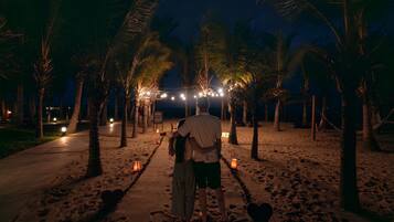 A nighttime beach scene with palm trees and string lights.