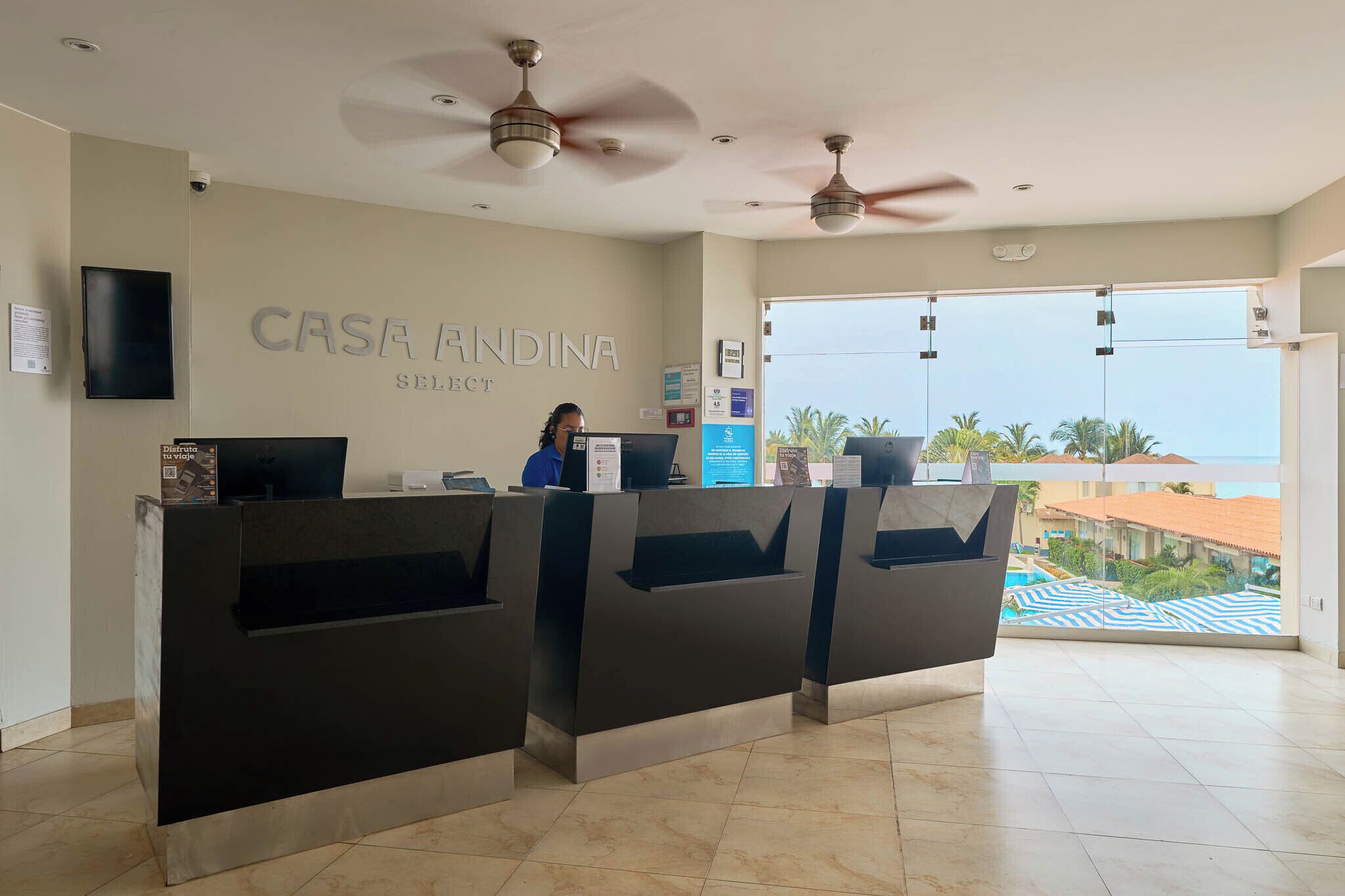 A reception area with a receptionist, a large window offering a view of the sea, and a ceiling fan.
