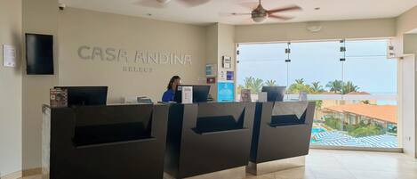 A reception area with a receptionist, a large window offering a view of the sea, and a ceiling fan.