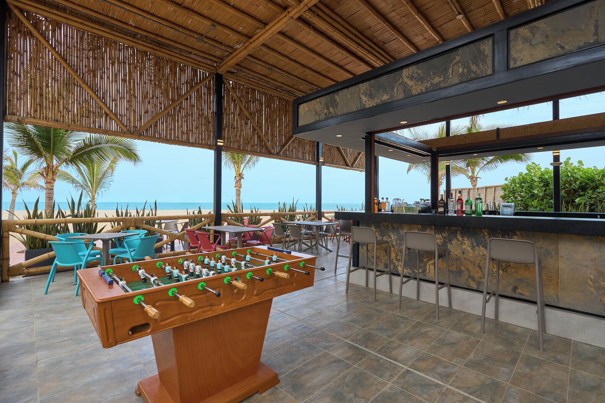 An outdoor bar area with a foosball table, seating, and a view of the beach.