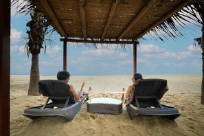 Two people relaxing on wicker lounge chairs under a thatched roof, with a beach and ocean view. - Casa Andina Select Zorritos Tumbes (Bocapan)