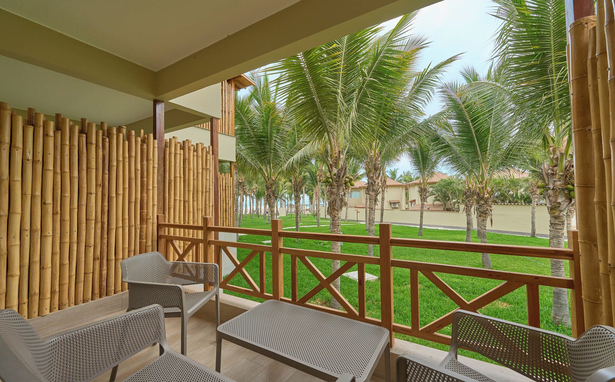 A covered outdoor seating area with bamboo walls, a view of palm trees, and a grassy lawn.