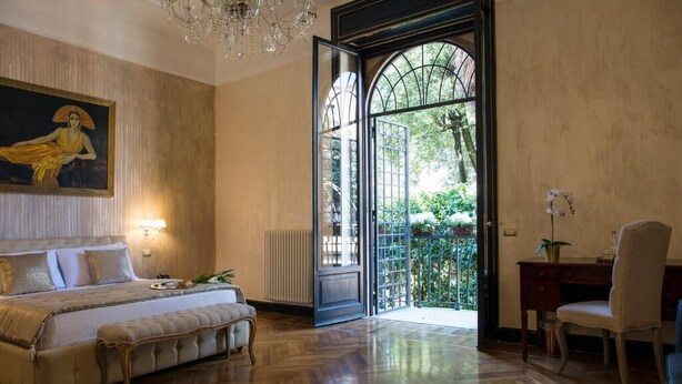 A bedroom with a large bed, a desk, and a chair. There is a painting on the wall and a chandelier above the bed. - Contessa Arrivabene Antica Dimora (Rome)