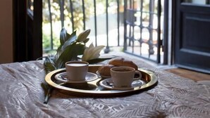 A bed with a tray of breakfast items, a cup of coffee, and a pastry, with a view of a balcony and greenery outside. - Contessa Arrivabene Antica Dimora (Rome)