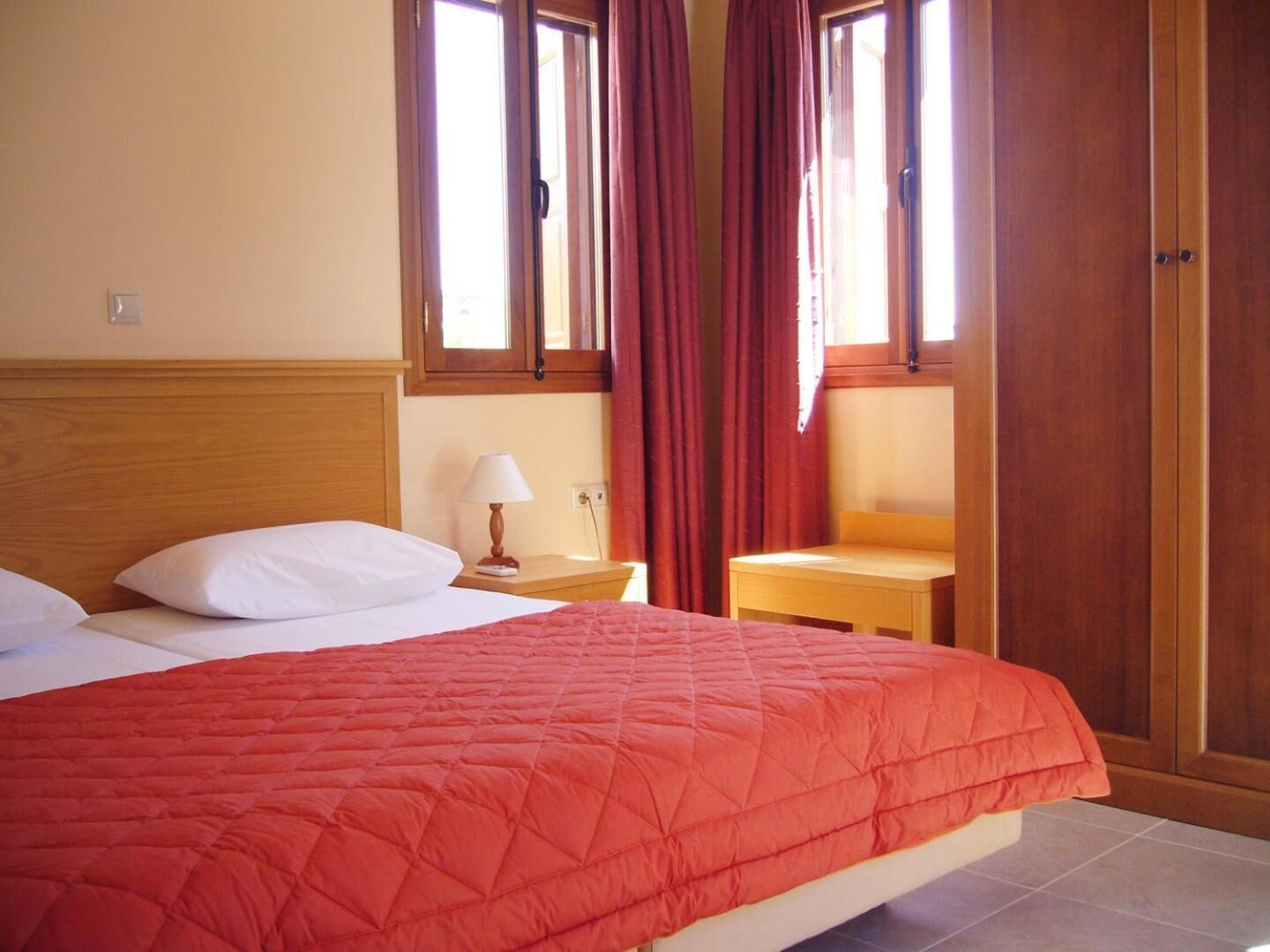 Habitación de hotel con cama, mesita de noche, lámpara y armario de madera.
