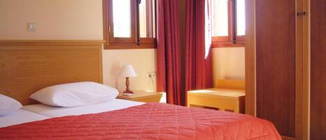 Habitación de hotel con cama, mesita de noche, lámpara y armario de madera.