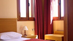 Et hotelværelse med en seng, et natbord, en lampe og et vindue med gardiner.