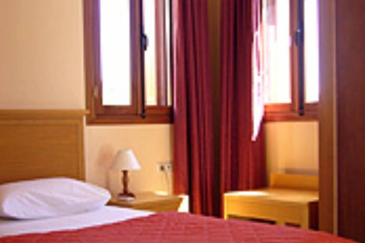 Quarto de hotel com cama, mesa de cabeceira, abajur e janela com cortinas.