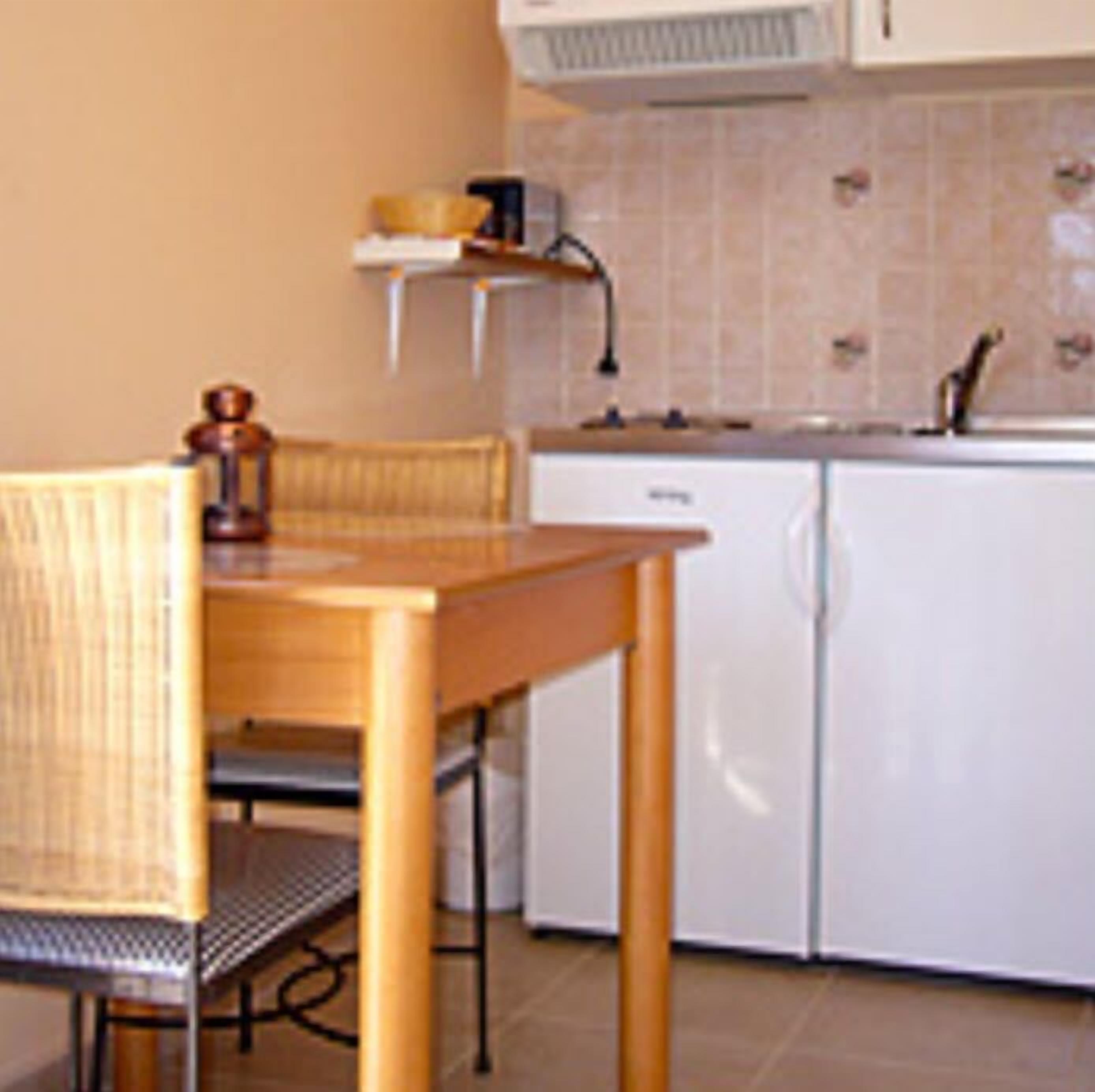 Une cuisine compacte avec une table et des chaises en bois, un lave-vaisselle blanc et un dosseret carrelé.
