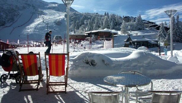 Zona nevada al aire libre con un telesilla de fondo, un ascensor de esquí y un edificio con un letrero que dice "Ski School".