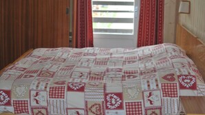 Una cama con colcha de varios diseños, cabecera de madera y ventana con cortinas.