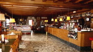 Interior de un restaurante con suelo de baldosas de piedra, mobiliario de madera y una zona de bar con estantes llenos de botellas.
