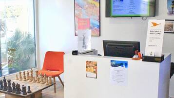 Zona de recepción con un tablero de ajedrez, una computadora y un cartel que indica bienvenida prioritaria.