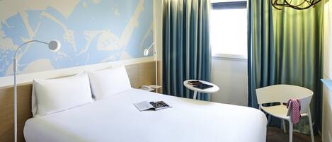 Una habitación de hotel con cama, escritorio, silla, lámpara y ventana con cortinas.