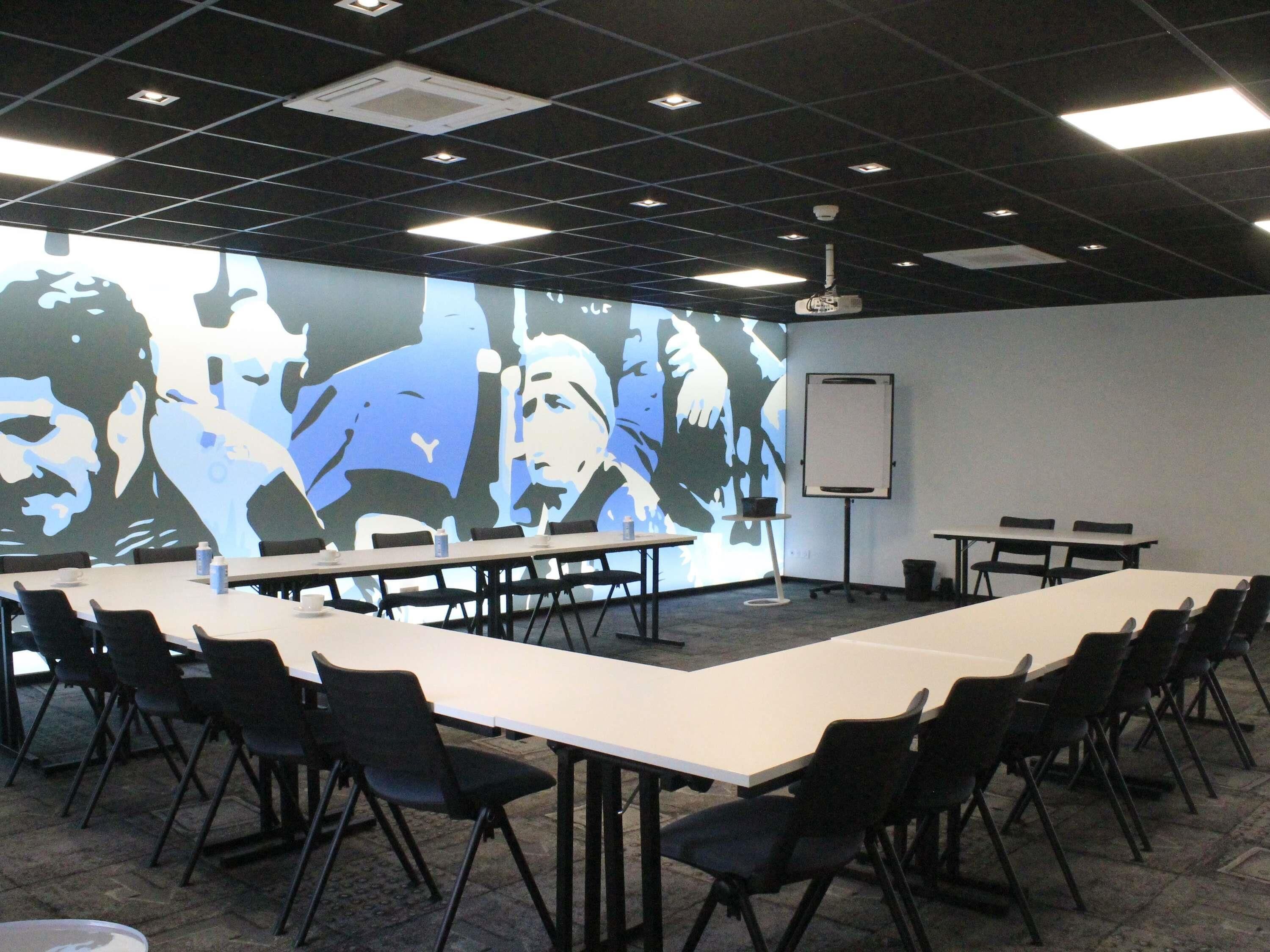 Ett konferensrum med ett långt bord, stolar, en projektorduk och en whiteboard.