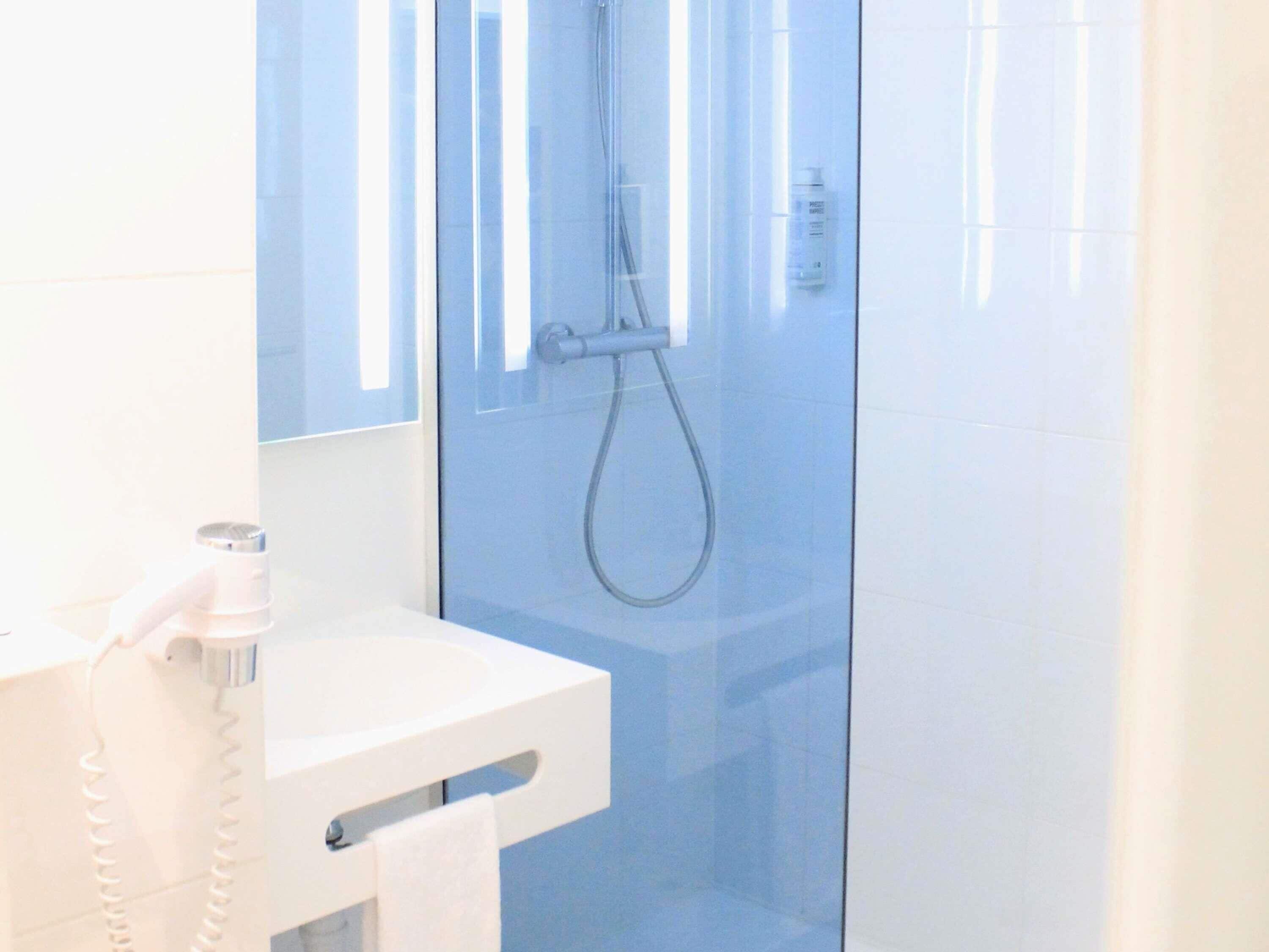 A modern bathroom with a glass shower enclosure, a white sink, and a towel rack.