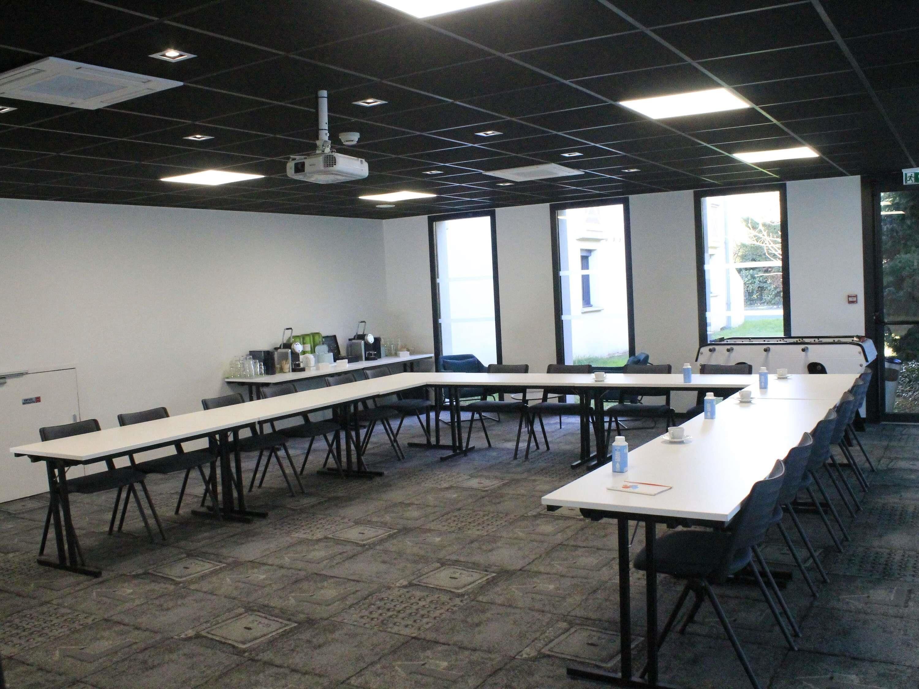 Un salón de conferencias con una larga mesa, sillas, un proyector y ventanas amplias.