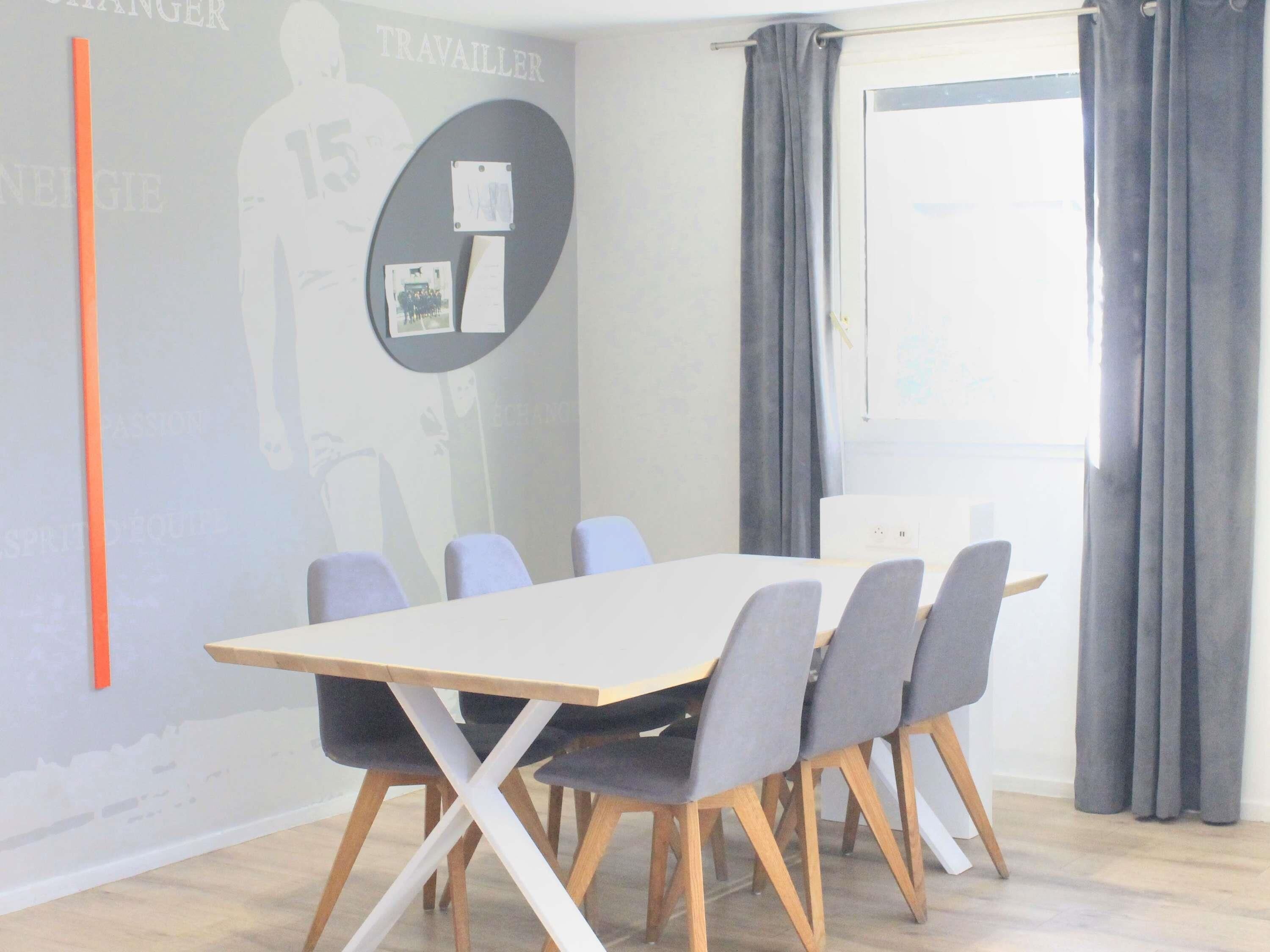 Uma sala de conferências com uma mesa comprida, seis cadeiras e uma tela de projetor.