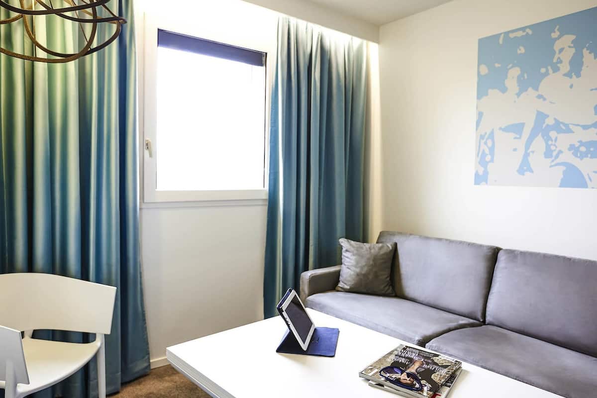 Ein modernes Wohnzimmer mit einem weißen Couchtisch, einem grauen Sofa, einem weißen Sessel und einem Fenster mit blauen Vorhängen.