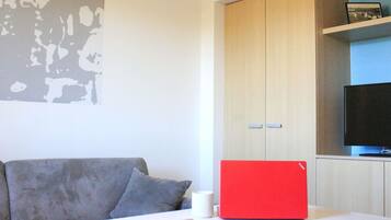 A modern living room with a grey sofa, a red laptop on a white table, and a TV on a shelf.