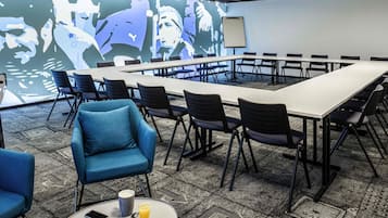 A conference room with a long table, chairs, a projector screen, and a large wall mural.