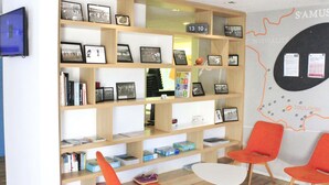A room with a bookshelf filled with books and framed photos, a white table, and two orange chairs. - ibis Styles Toulouse Nord Sesquières (Toulouse)
