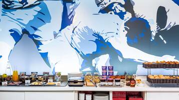A breakfast buffet with various food items and a large abstract painting on the wall.