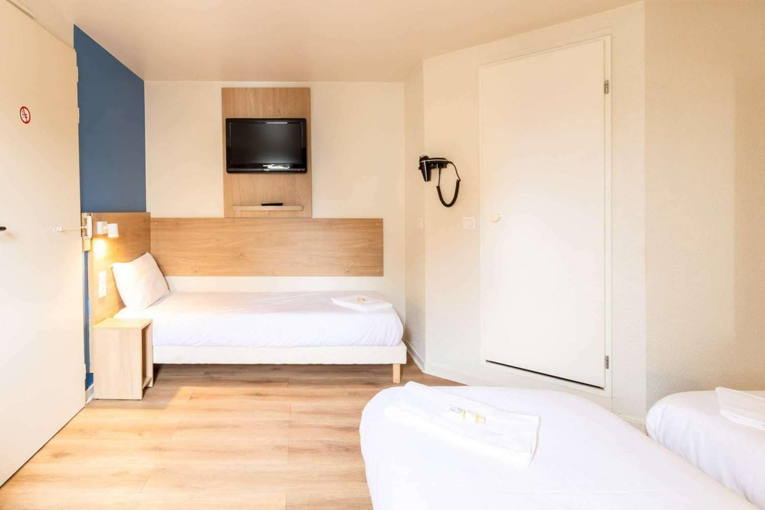 A hotel room with a bed, a TV mounted on the wall, a bedside table with a lamp, and a wardrobe.