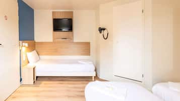 A hotel room with a bed, a TV mounted on the wall, a bedside table with a lamp, and a wardrobe.