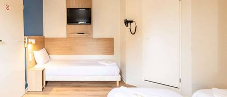 A hotel room with a bed, a TV mounted on the wall, a bedside table with a lamp, and a wardrobe.