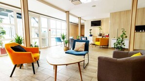 A modern hotel lobby with a large open space, seating areas, and potted plants. - Brit Hotel Rouen Barentin (Barentin)
