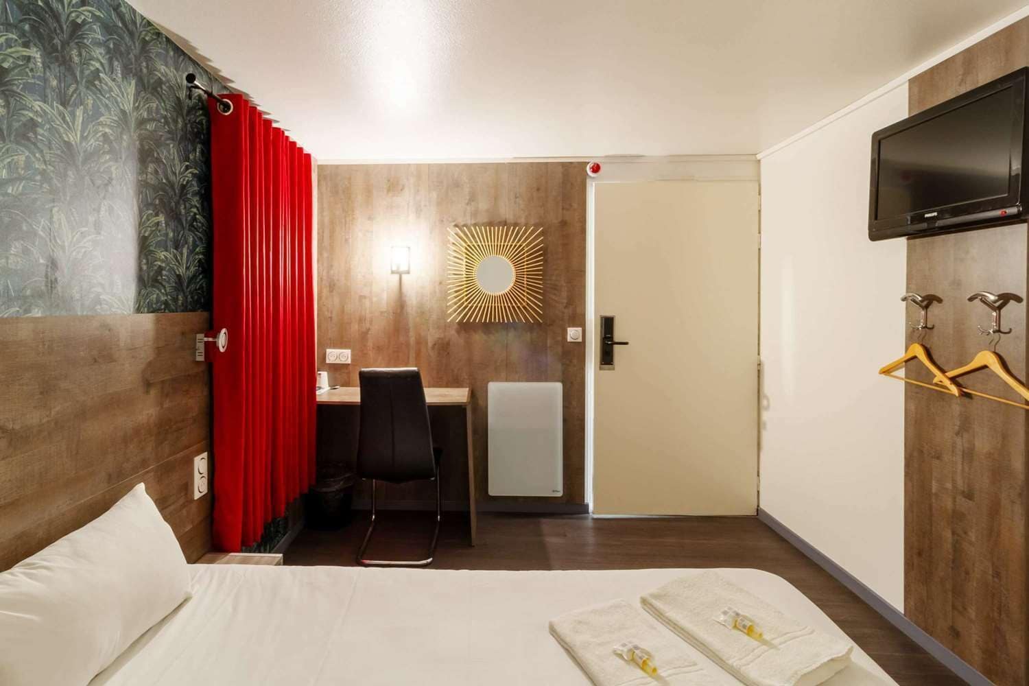 A hotel room with a bed, a desk, a chair, a TV, and a shower area.