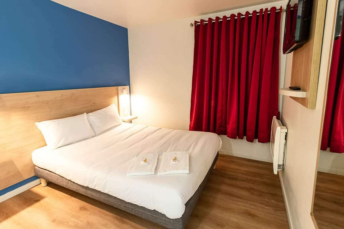 A neatly made bed with white linens, a wooden headboard, and a red curtain.