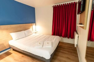 Una cama bien hecha con sábanas blancas, cabecera de madera y cortina roja.