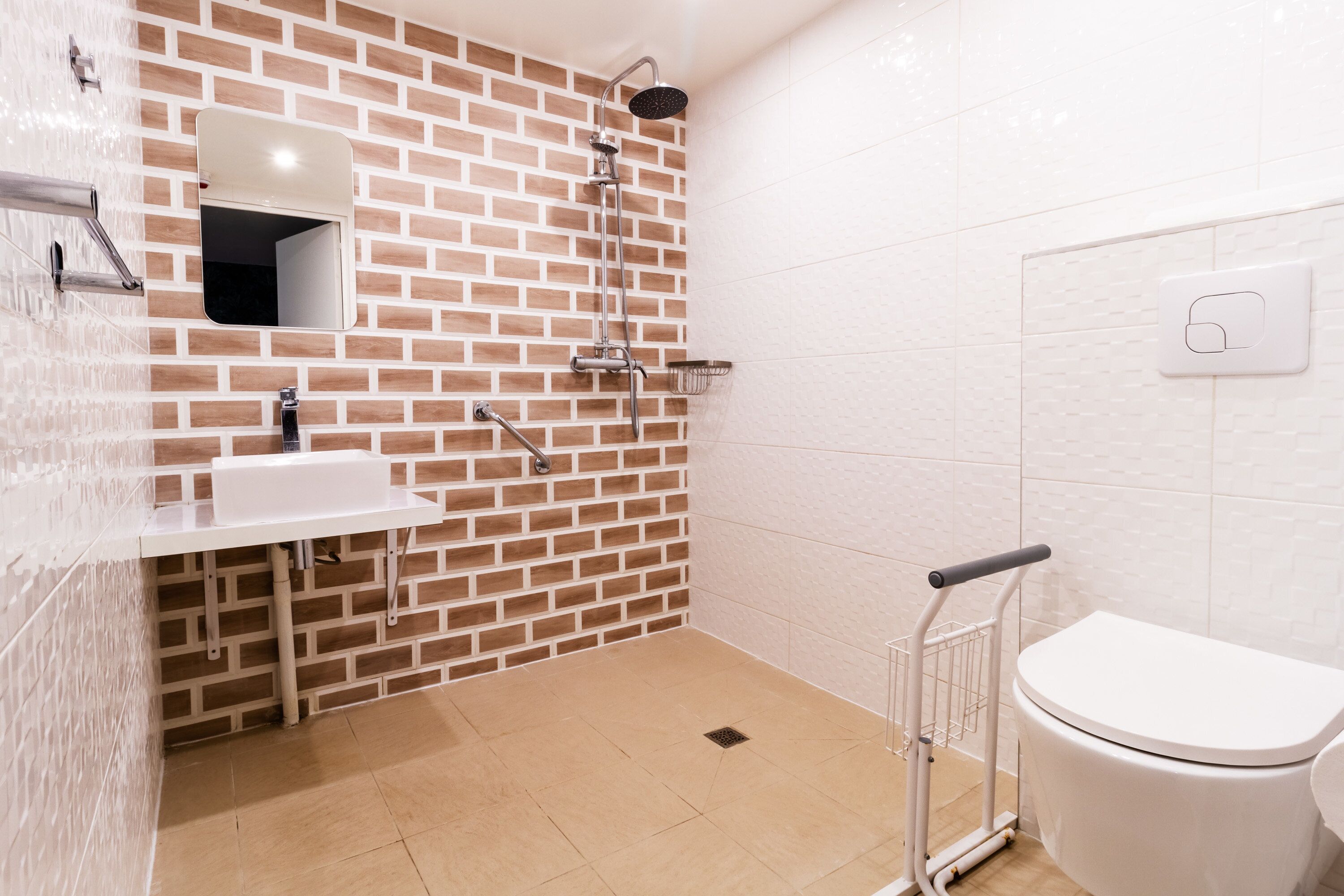A modern bathroom with a brick-patterned wall, a white sink, a toilet, and a shower with a handheld showerhead.