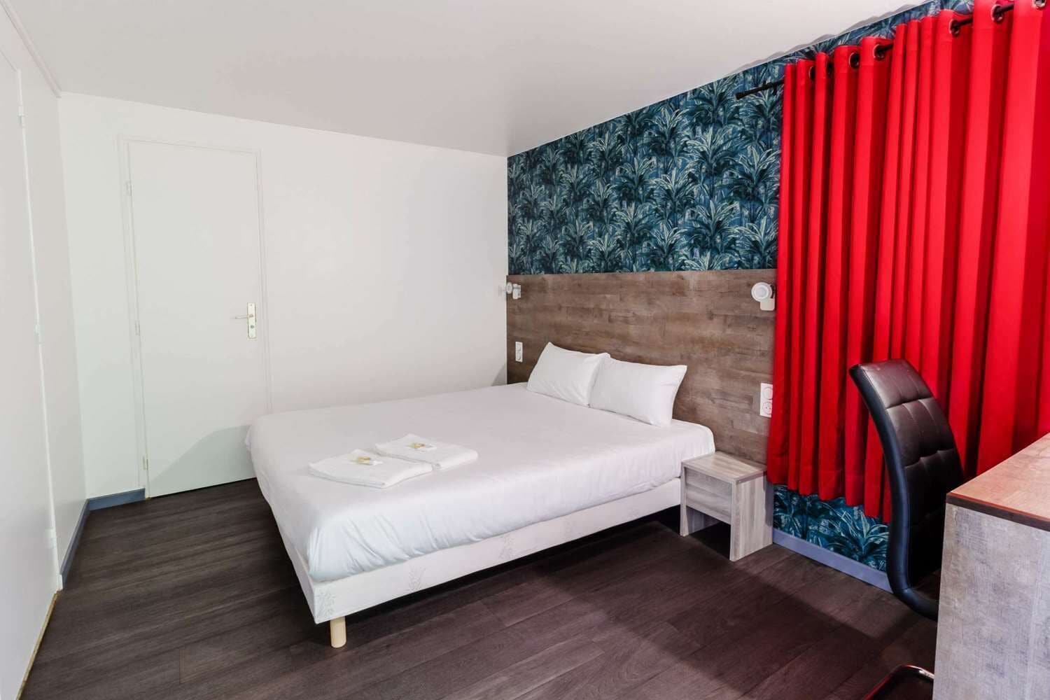 Una habitación de hotel con cama, escritorio, silla y cortina roja.