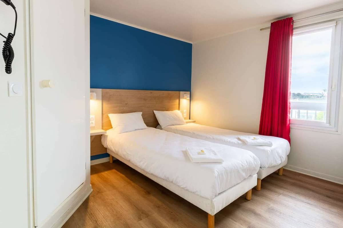 A double bed room with a wooden headboard, white bedding, and a red curtain.