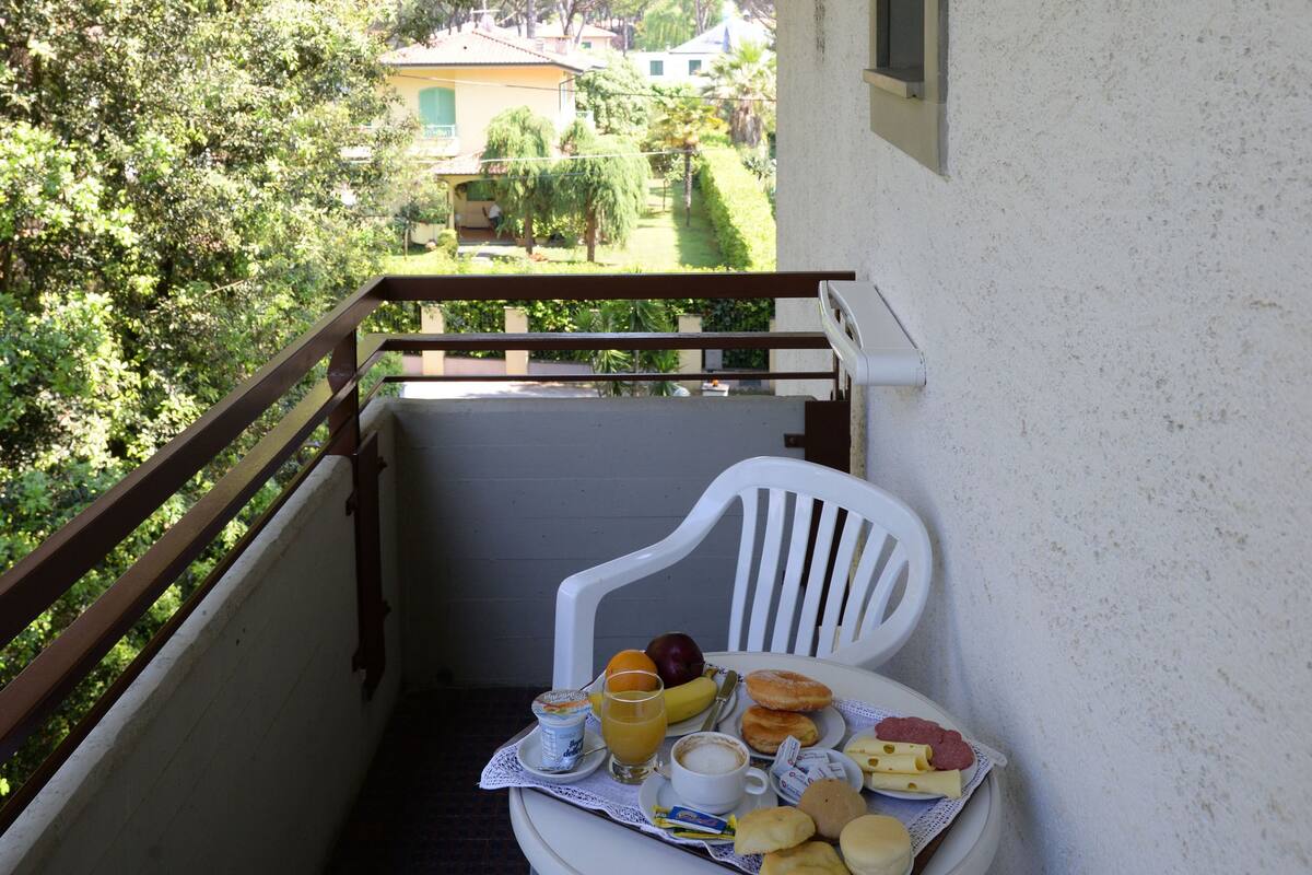 Un balcon avec une table préparée pour le petit-déjeuner, comprenant une boisson, des viennoiseries et un sandwich.