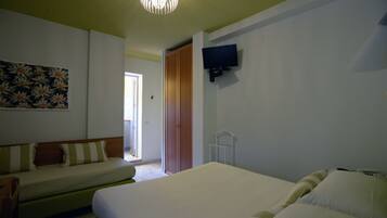 A hotel room with a bed, a sofa, a television mounted on the wall, and a door leading to a balcony.
