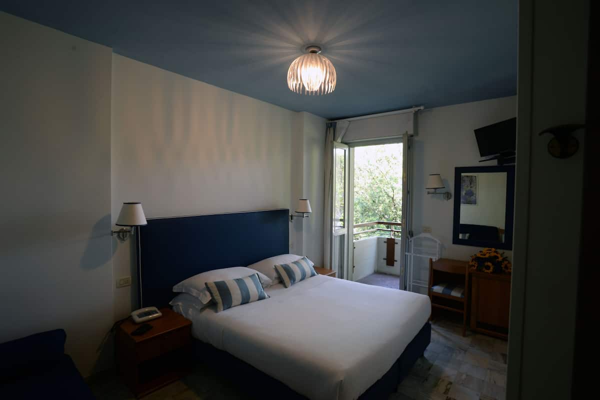 Une chambre à coucher avec un lit, des lampes de chevet, une table de chevet, une commode, un miroir et une vue sur le balcon.