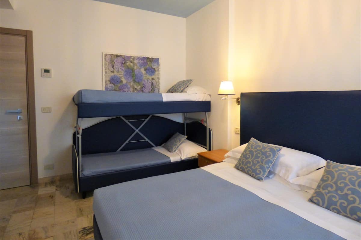 Une chambre d’hôtel équipée d’un lit superposé, d’un lit simple, d’une lampe de chevet et d’une œuvre d’art accrochée au mur.