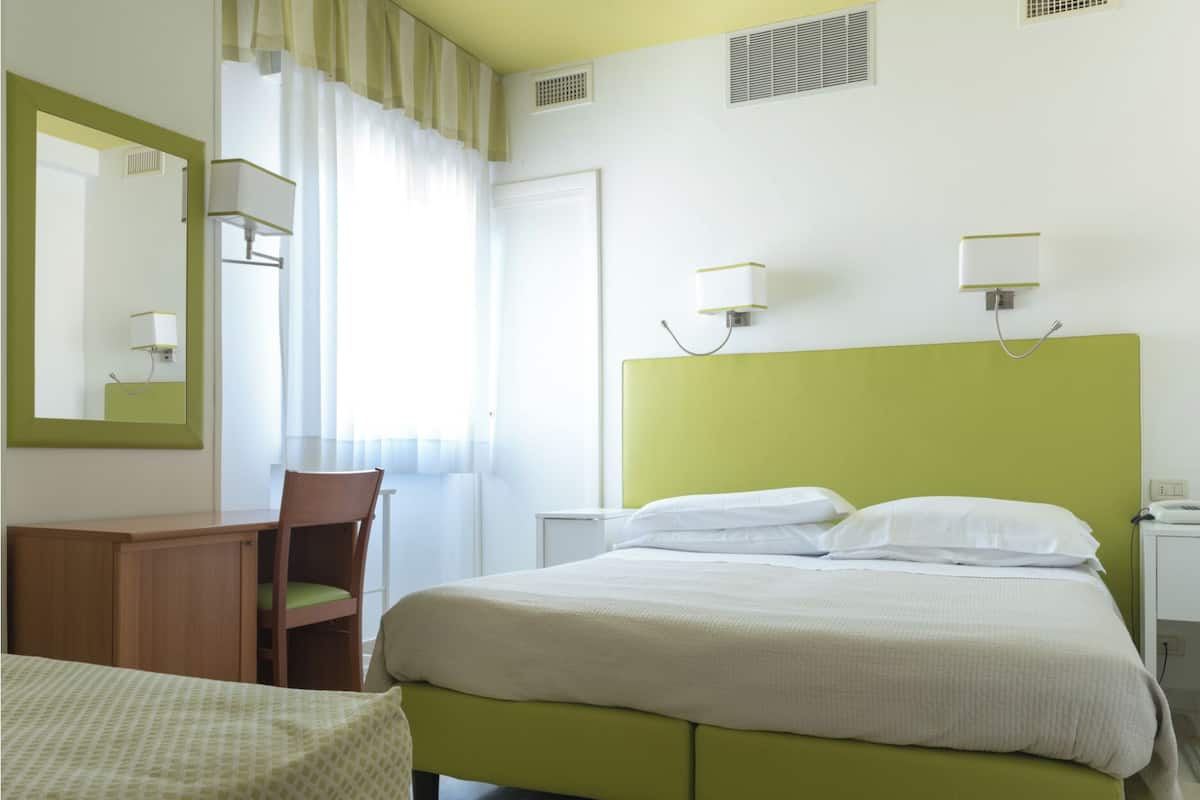 Une chambre d’hôtel avec un lit, un bureau, une chaise et un miroir.