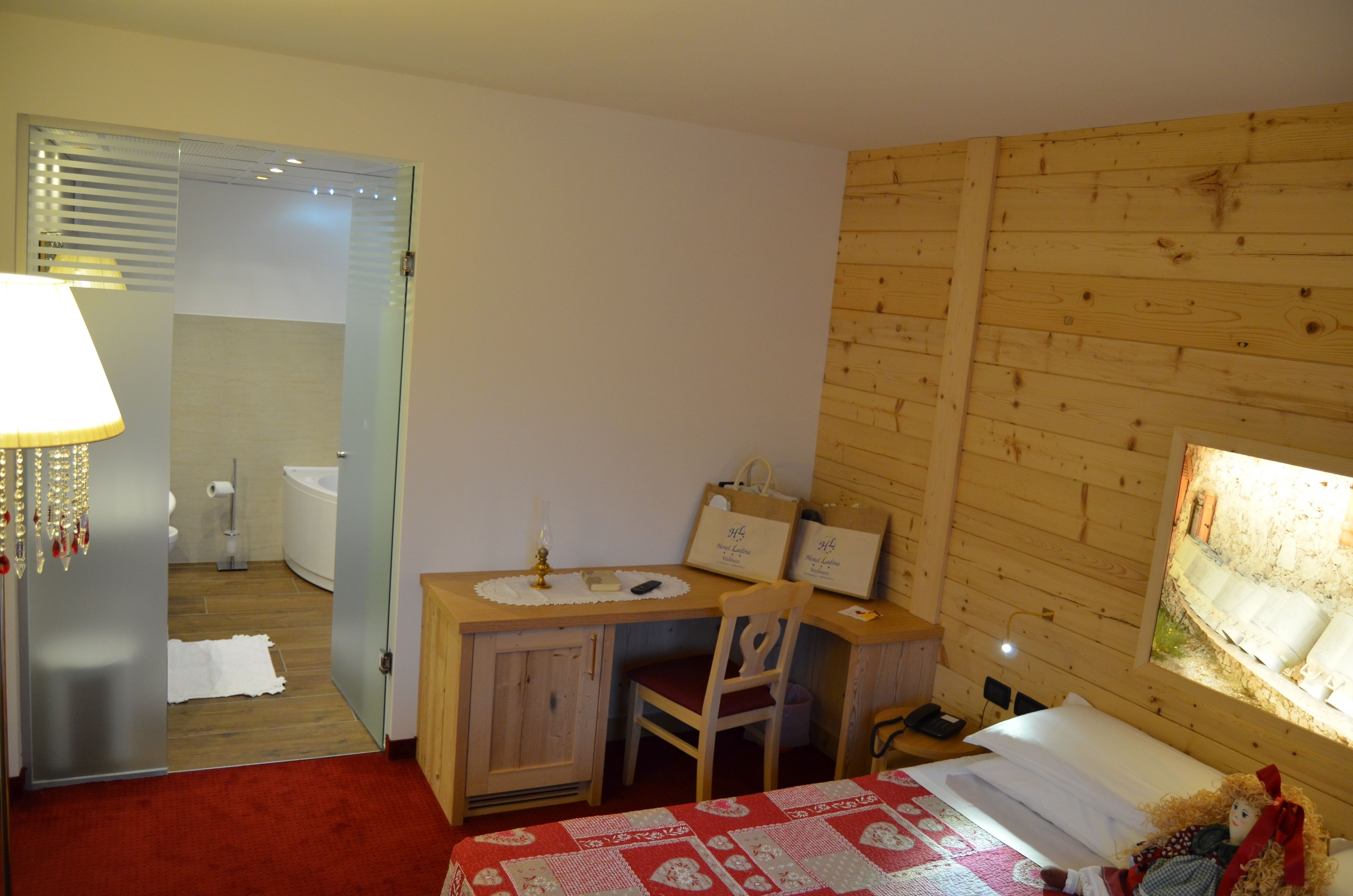 Una habitación con paneles de madera, una cama, un escritorio con una silla, una lámpara y una pequeña mesa con un marco de fotos.