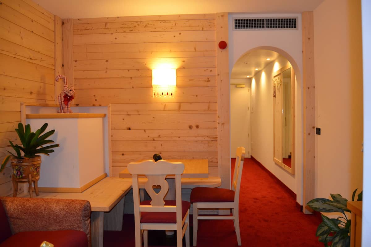 A cozy room with wooden walls, a small table, two chairs, a potted plant, and a red carpeted floor.