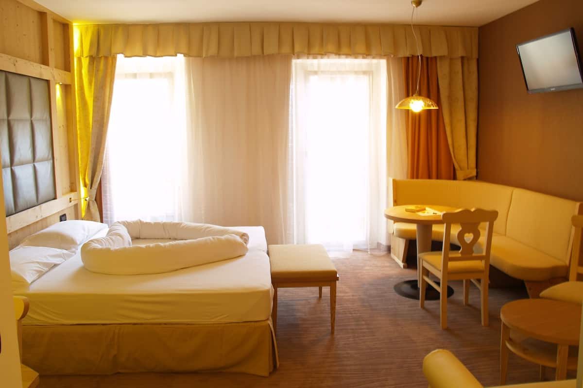 A hotel room with a bed, a desk, a chair, and a television on the wall.