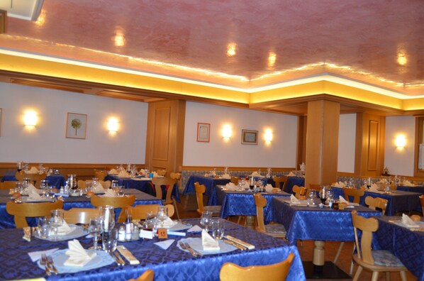 A banquet hall with tables set for dining, featuring blue tablecloths and wooden chairs. - Hotel Ladina (Campitello di Fassa)