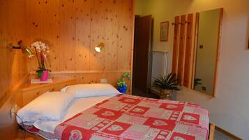Una camera da letto con rivestimento in legno, un letto, un comodino con un vaso di fiori, uno specchio e un termosifone.