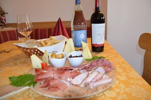 A table with a variety of cheeses, meats, and a bottle of wine, suggesting a meal setting. - Hotel Ladina (Campitello di Fassa)